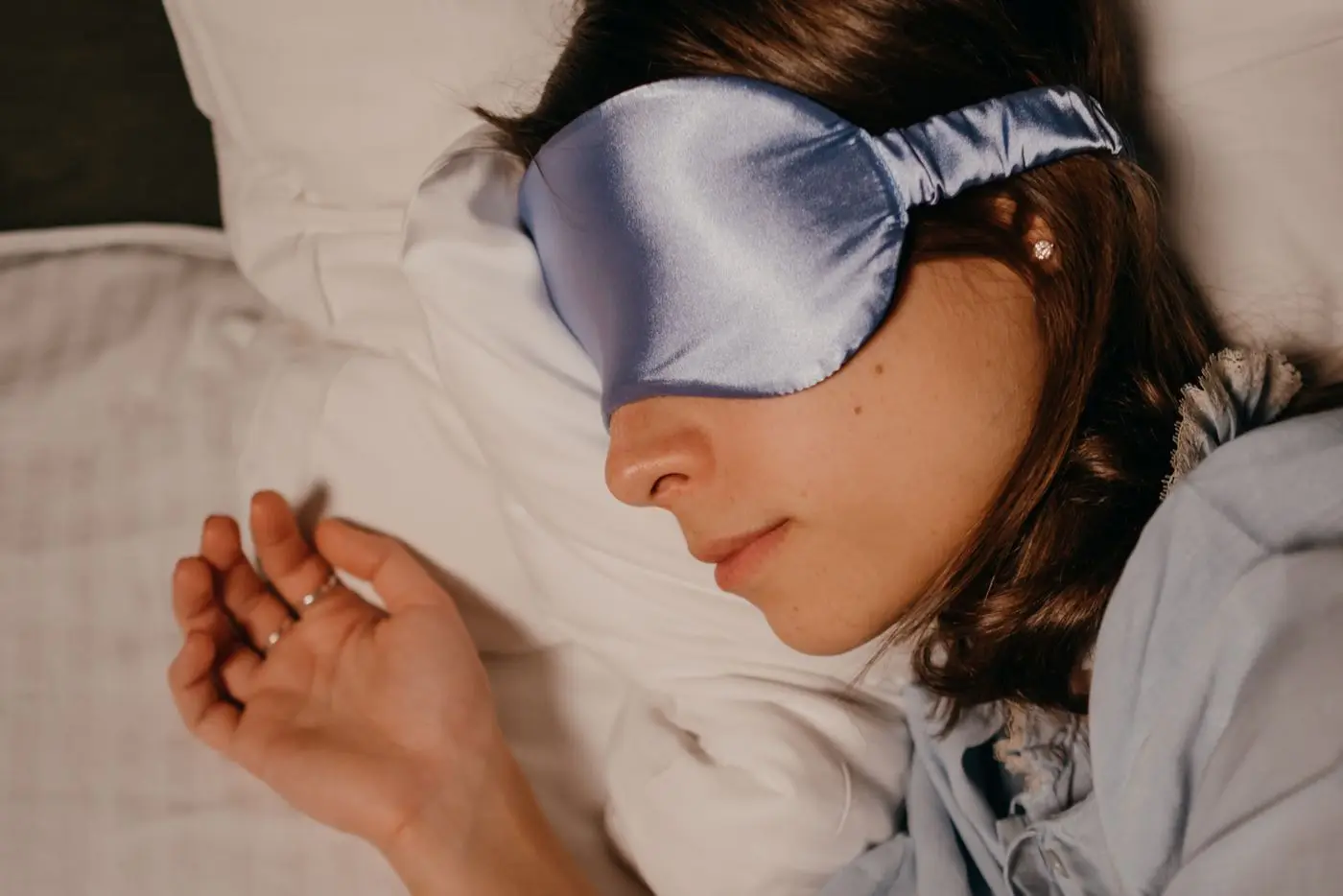 Kvinna som sover med sovmask i siden och håret utspritt över kudden