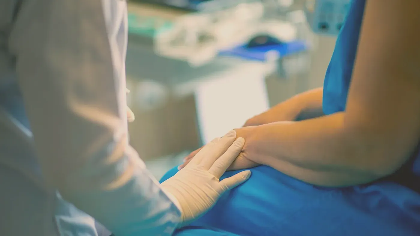 Läkares handskbeklädda hand som lugnande vilar på en patients hand